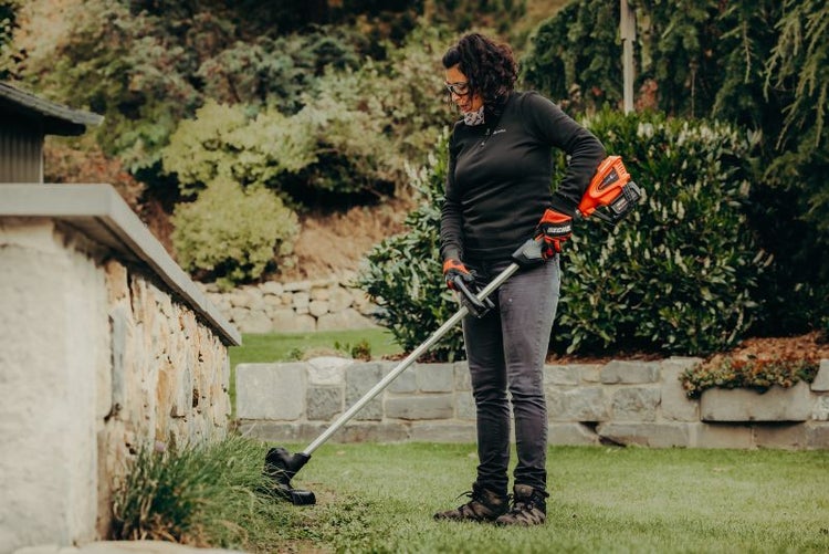 Frau benutzt Rasentrimmer im Garten zur Rasenpflege.