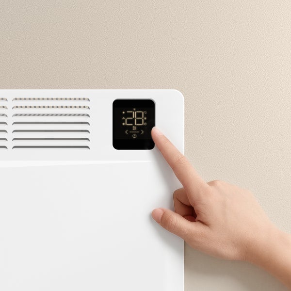 Nahaufnahme eines weißen Heizkörpers mit digitalem Display, das von einer Hand bedient wird