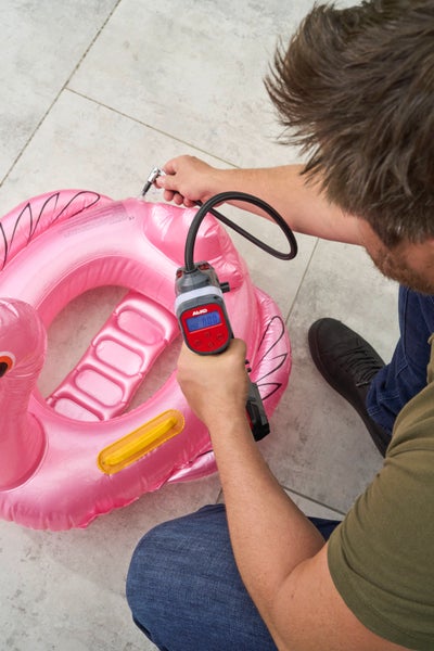 Person pumpt ein aufblasbares Wassertier in Flamingo-Form mit einem AL-KO Akku-Kompressor auf einer hellen Steinfläche auf.