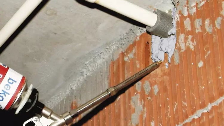 Applikation von Bauschaum zur Abdichtung einer Rohrdurchführung in einer Wand.