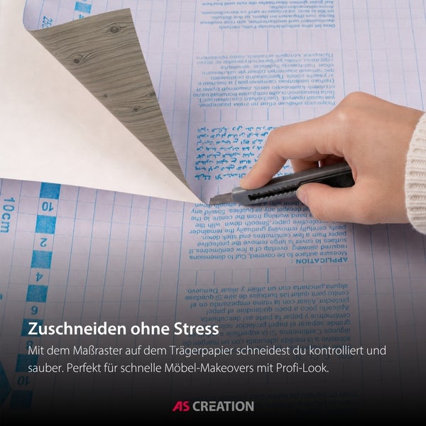 Zuschneiden einer selbstklebenden Folie in Holzoptik mit einem Cutter entlang des Maßrasters auf dem Trägerpapier. AS Creation Logo.