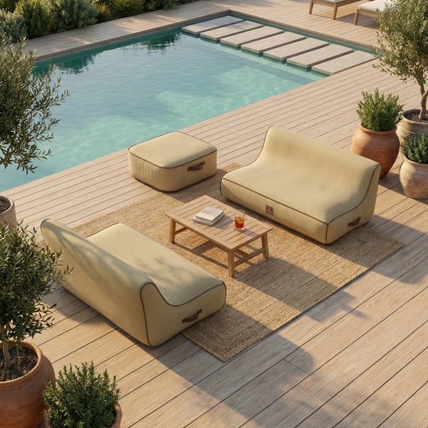 Moderner Außenloungebereich auf Holzterrasse am Pool mit zwei beigen Sesseln, einem Hocker, einem Holz-Couchtisch und einem Juteteppich.