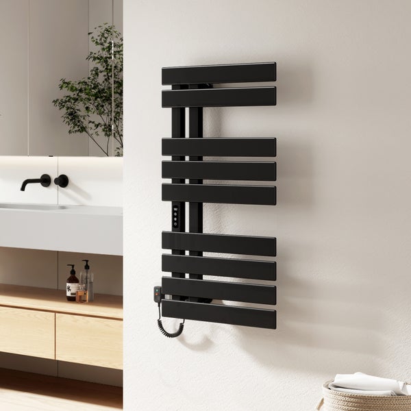 Schwarzer elektrischer Handtuchheizkörper an einer weißen Badezimmerwand neben einem Waschbecken und einem hellen Holzunterschrank.