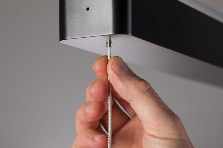 Hand justiert eine Deckenleuchte mit Seilaufhängung