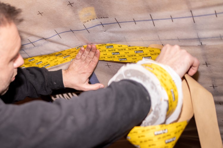 Eine Person bringt Prima EASY TAPE Klebeband auf einer Dampfbremsfolie zur Abdichtung an.