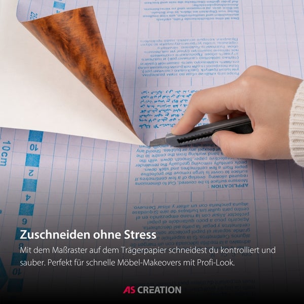 Selbstklebefolie in Holzoptik wird mit einem Cuttermesser auf dem Maßraster des Trägerpapiers zugeschnitten. AS Creation Logo.