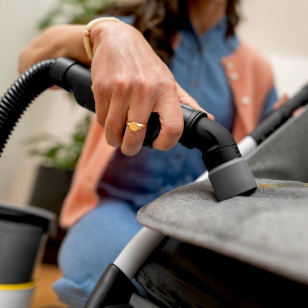 Frau reinigt ein graues Sofa mit einem Staubsaugeraufsatz