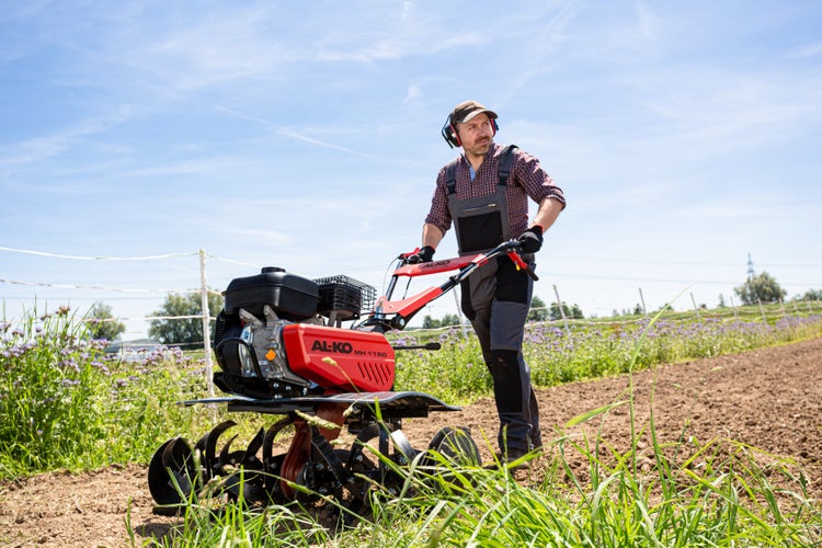 Ein Gärtner bedient eine AL-KO Motorhacke MH 1150 auf einem Feld während der Gartenarbeit.