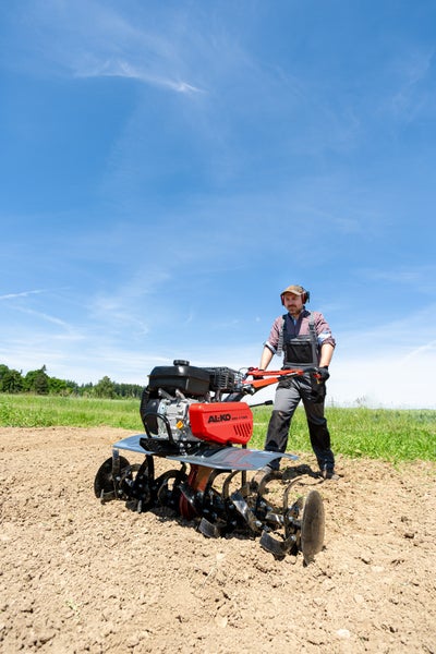 Ein Gärtner verwendet eine AL-KO Motorhacke MH 1150 zur Bodenbearbeitung auf einem Feld unter freiem Himmel.