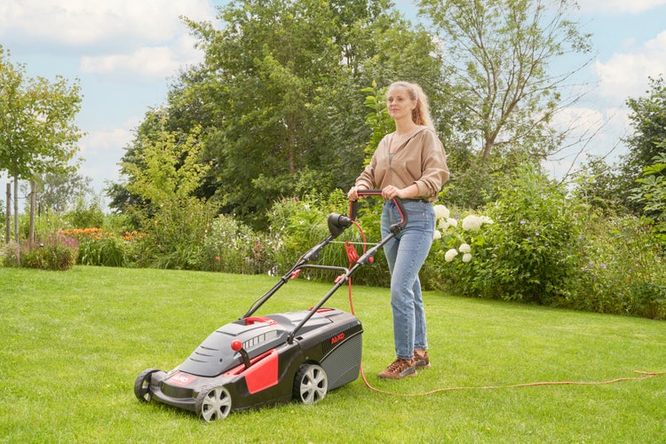Eine Frau mäht mit einem elektrischen AL-KO Rasenmäher in einem Garten den Rasen.