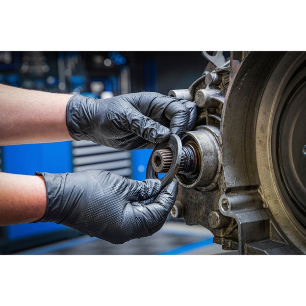 Mechaniker in Arbeitshandschuhen montiert eine Unterlegscheibe an einer Getriebewelle im Werkstattbereich.