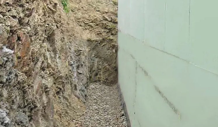 Nahaufnahme von Gebäudedämmung neben einem Erdaushub mit Steinen.