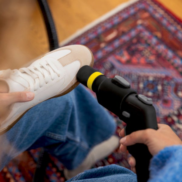 Person reinigt Schuh mit Dampfreiniger auf Teppich