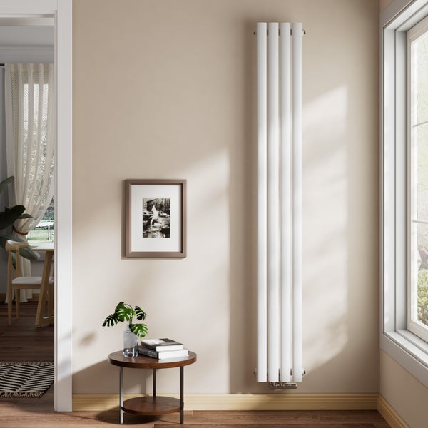 Vertikaler Röhrenheizkörper in einem hellen, modern eingerichteten Wohnzimmer neben einem Fenster und einem Beistelltisch.