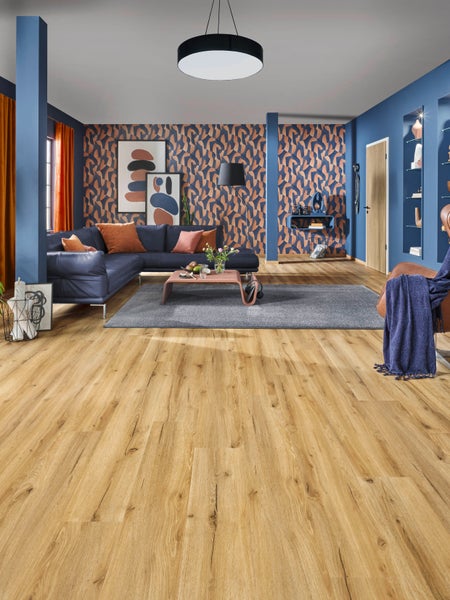 Modernes Wohnzimmer mit Bodenbelag in Eichenoptik, blauem Ecksofa, grauem Teppich und gemusterter Tapete an den Wänden.