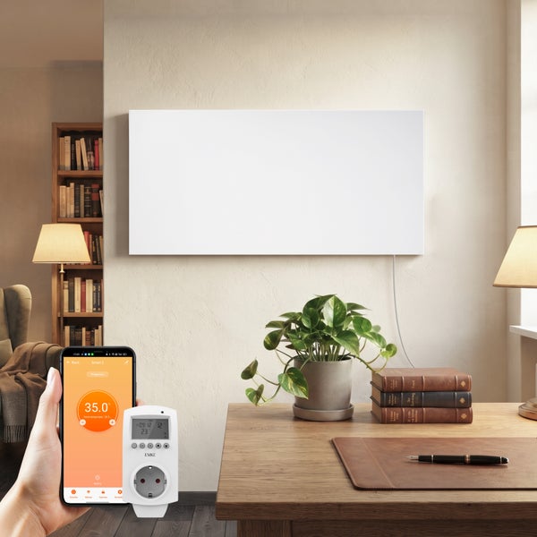Eine Infrarotheizung an einer Wohnzimmerwand mit Smartphone-Steuerung und einem intelligenten Zwischenstecker für die Temperaturregelung.