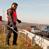 Mann mit Rasentrimmer an einer Leitplanke.