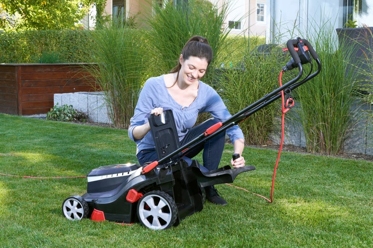 Eine Frau bedient einen Elektro Rasenmäher auf einem Gartenrasen.