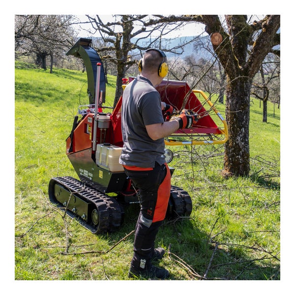 Garten Szene mit Raupenhäcksler im Einsatz, bedient von Person mit Schutzausrüstung.