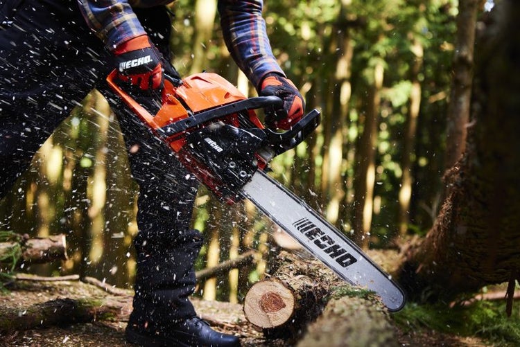 Eine Person sägt mit einer Motorsäge einen Baumstamm im Wald.