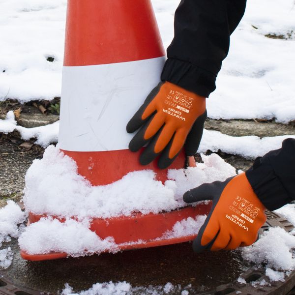 Eine Person mit Winter Grip Handschuhen hantiert mit einem Verkehrskegel im Schnee.
