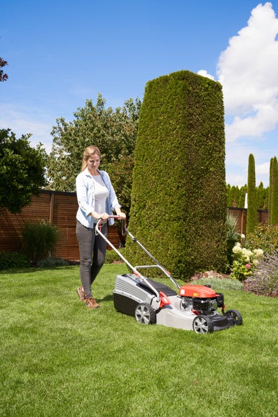 Eine Frau mäht den Rasen in einem Garten mit einem Benzinrasenmäher an einem sonnigen Tag.