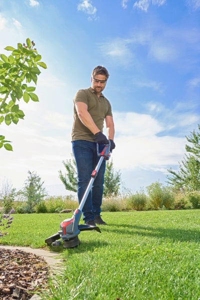 Ein Mann nutzt einen Akku-Rasentrimmer zum Schneiden der Rasenkanten in einem sonnigen Garten.