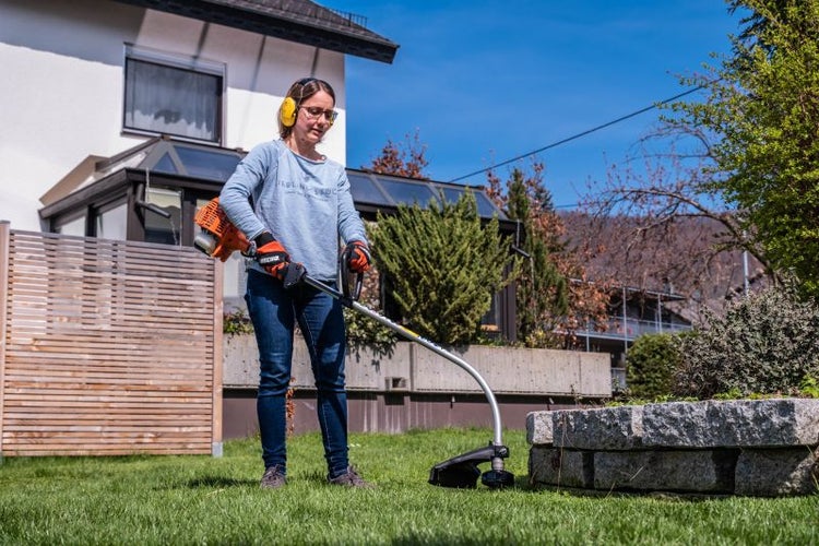 Frau mit gelben Ohrenschützern, die einen Rasentrimmer im Garten benutzt