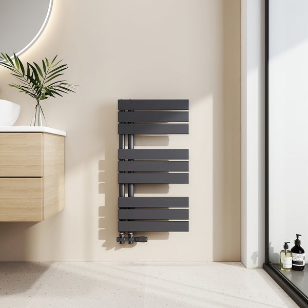 Moderner asymmetrischer Badheizkörper aus Metall an einer Wand neben einem Waschtisch aus Holz in einem hellen Badezimmer.