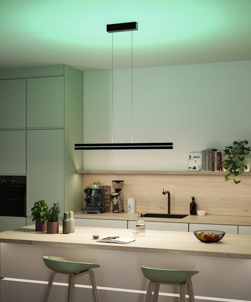 Moderne schwarze lineare LED-Pendelleuchte in einer organisierten Küche, hängend über einer Kücheninsel aus hellem Holz mit Barhockern.