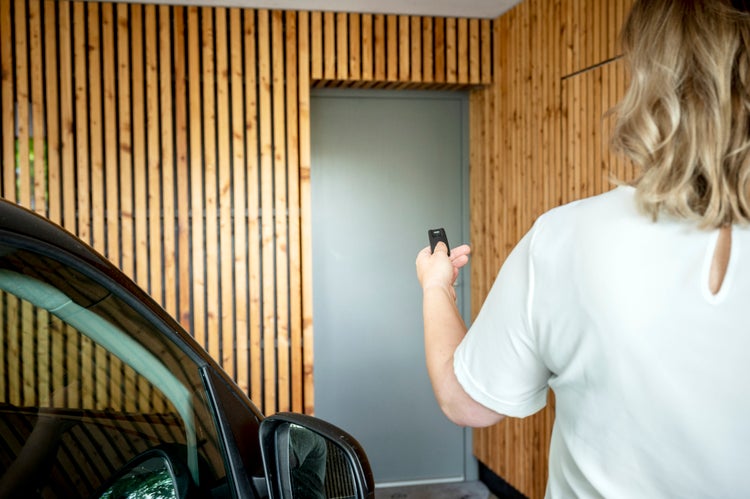 Person bedient einen Handsender vor einer Tür mit Holzverkleidung neben einem Auto.