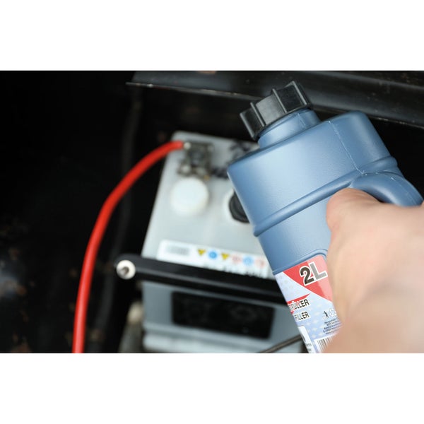 Ein Mann füllt Kühlflüssigkeit aus einem zwei Liter Behälter in ein Auto.