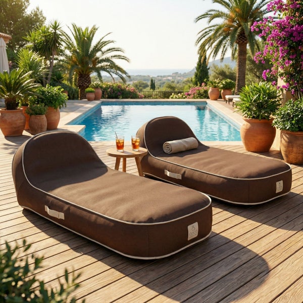 Zwei braune Outdoor-Lounge-Sitzsäcke auf einer Holzterrasse neben einem Pool mit Palmen und Topfpflanzen in heller Umgebung.