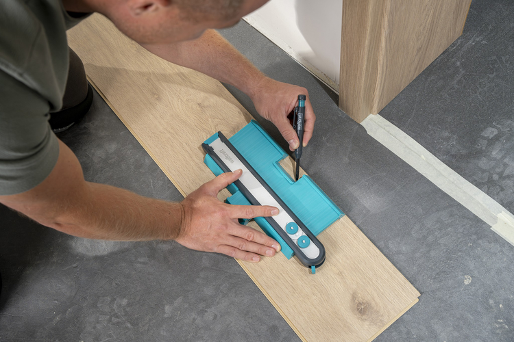 Person überträgt mit einer Wolfcraft Konturenlehre die Form einer Türzarge auf eine Laminatdiele zum präzisen Zuschneiden.