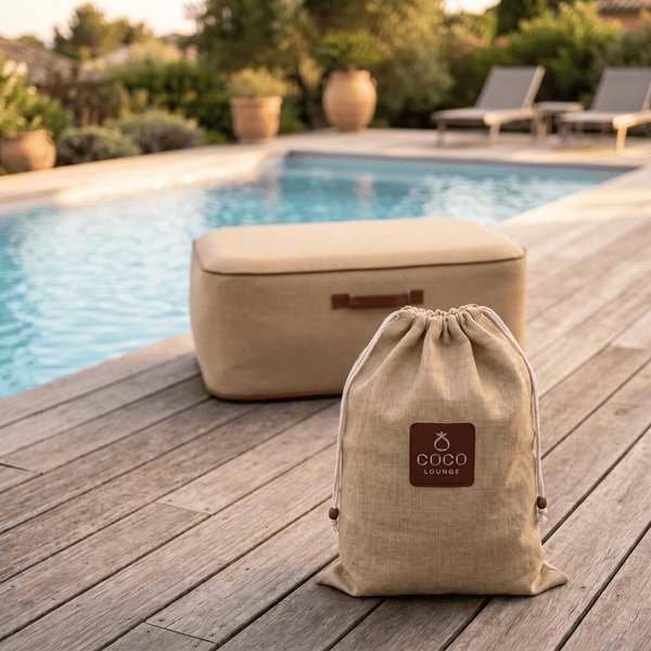 Beutel mit Kordelzug mit Coco Lounge Logo und rechteckiger Outdoor-Hocker auf einem Holzdeck am Pool in einem hellen Außenbereich.