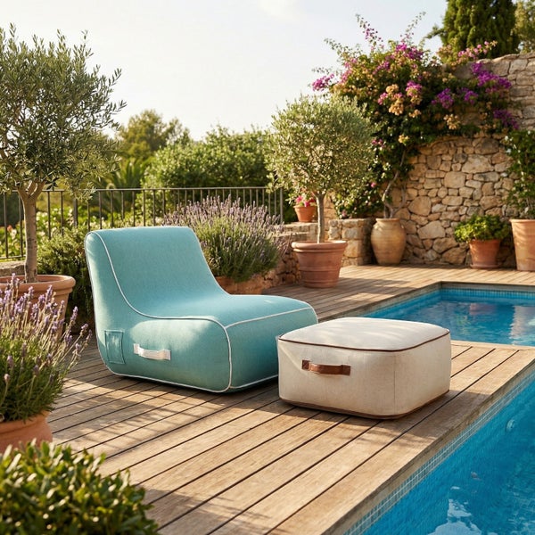 Moderner Außenbereich mit einem blauen Sitzsack-Sessel und einem beigen Hocker auf einer Holzterrasse am Pool, umgeben von Pflanzen.