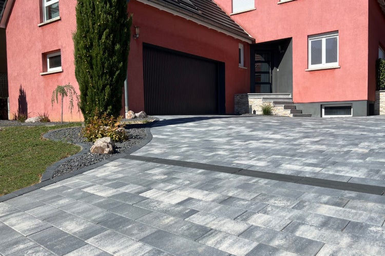 Moderne Hauseinfahrt mit rechteckigen Pflastersteinen aus Beton in Grau-Weiß-Nuancierung und dekorativer Gartengestaltung mit Kies.