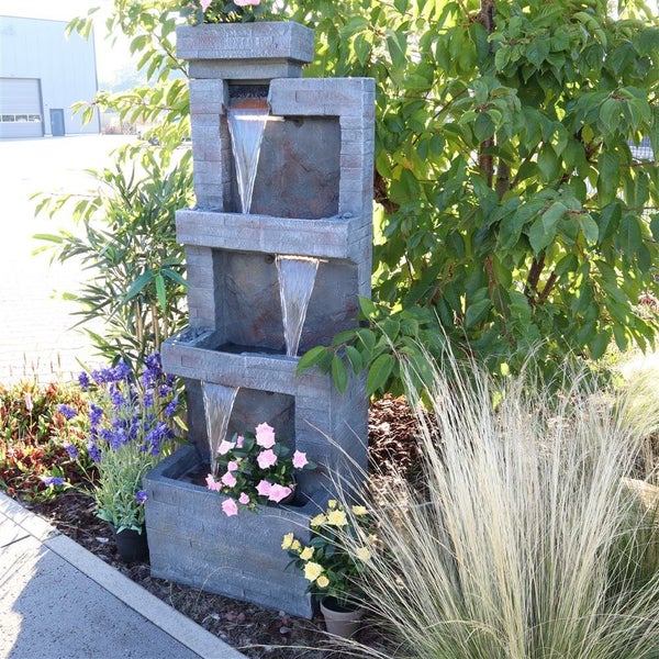 Mehrstufiger Gartenbrunnen aus Stein mit Wasserfluss und Bepflanzung.