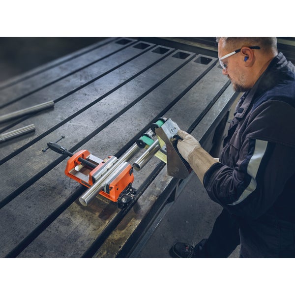 Handwerker schleift ein Metallrohr mit einem Bandschleifer, eingespannt in einen Schraubstock auf einem Werktisch.