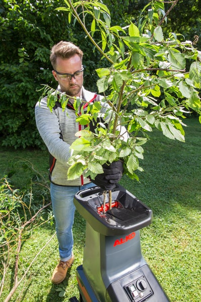 Ein Mann mit Schutzbrille und Handschuhen führt Äste in einen AL-KO Gartenhäcksler im Garten ein.