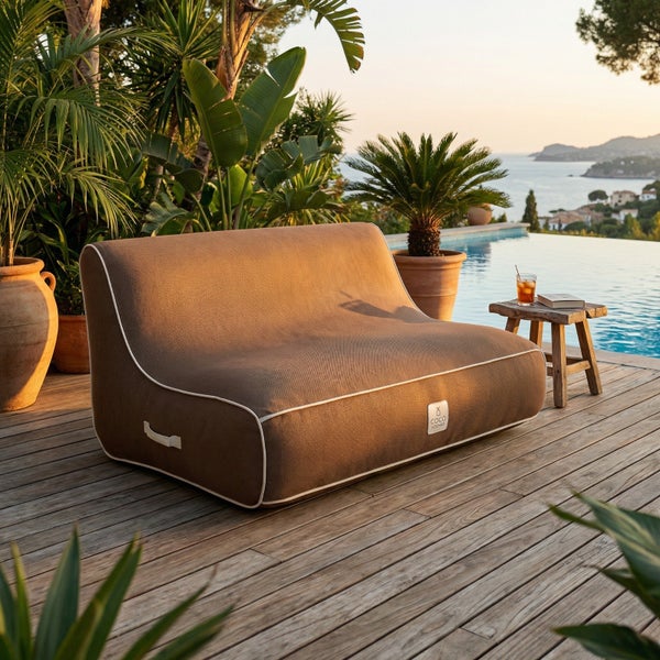 Outdoor-Sitzsack-Sofa aus grobem Stoff auf einer Holzterrasse am Pool mit Meerblick. Helle Atmosphäre mit tropischen Pflanzen.