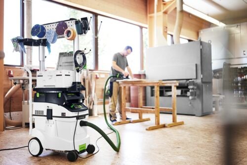 Mobiles Absaugmobil mit Workcenter in einer hellen Werkstatt, verbunden mit einem Schleifgerät an einer Hobelbank aus Holz.