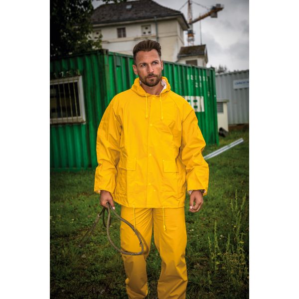 Mann in gelber Regenjacke und Regenhose vor Gebäude und Baucontainern