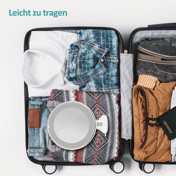 Geöffnete Reisekoffer gefüllt mit Kleidung und Kosmetikspiegel