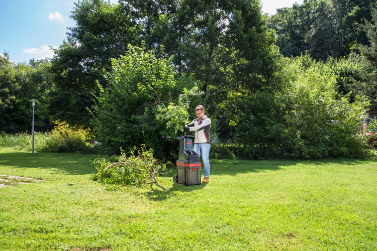 Mann bedient einen Elektro-Leisehäcksler im Garten, um abgeschnittene Äste zu zerkleinern.