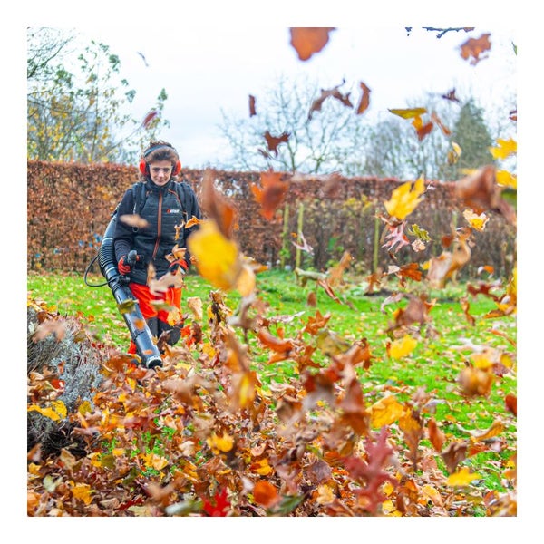Eine Person benutzt einen Laubbläser im Garten, um Herbstlaub zu entfernen.
