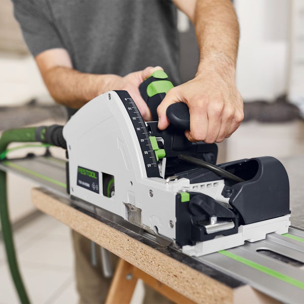 Festool Tauchsäge TSV 60 KEBQ mit Vorritzer auf Führungsschiene beim Schneiden einer Holzplatte auf Sägeböcken.