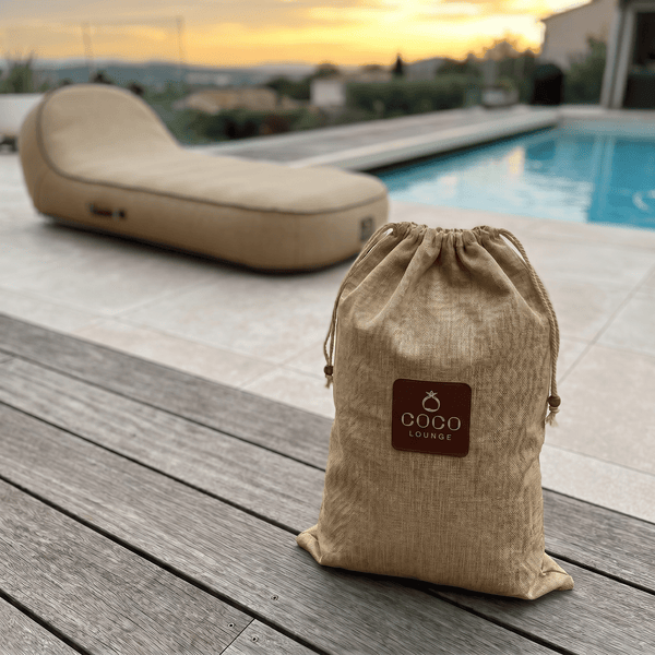 Kordelzugbeutel aus Textil mit Coco Lounge Logo auf einer Holzterrasse neben einem Pool und einer Gartenliege.