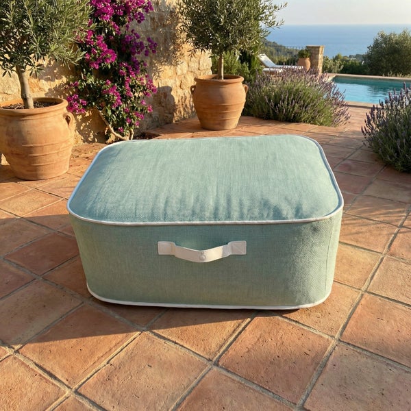 Rechteckiger Outdoor-Pouf in Mintgrün mit Tragegriff auf einer Terrasse aus Terrakotta-Fliesen neben einem Pool und Olivenbäumen.