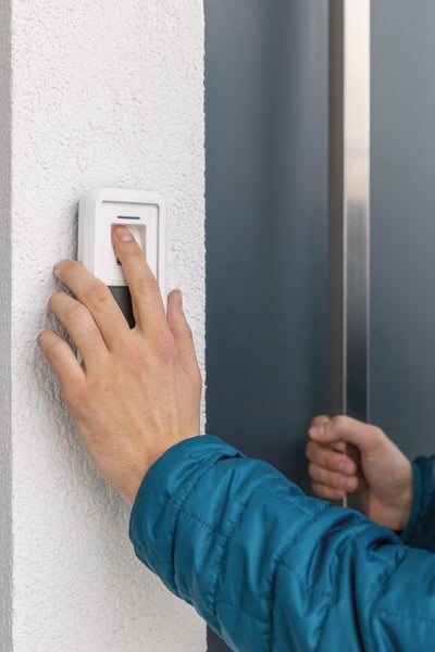 Person bedient einen Fingerabdruckscanner an einer Außenwand neben einer Haustür.